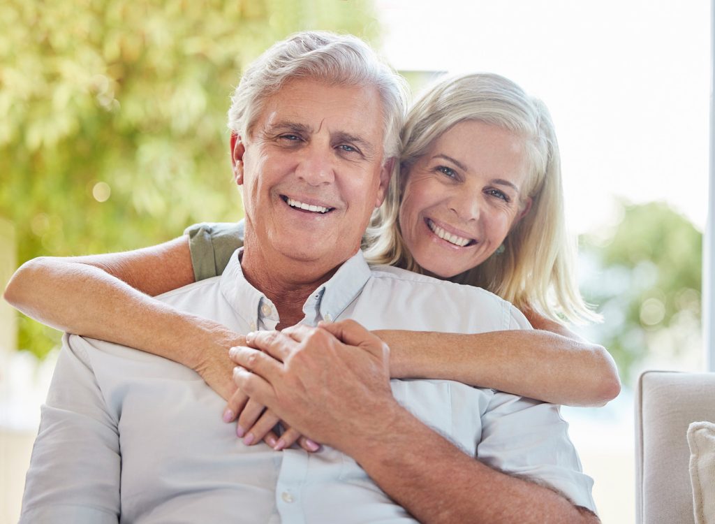 Senior,Couple,,Portrait,And,Hug,On,Sofa,In,Home,,Happy