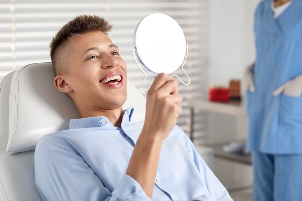 Happy,Young,Man,With,Mirror,In,Clinic,,Closeup.,Dental,Veneers