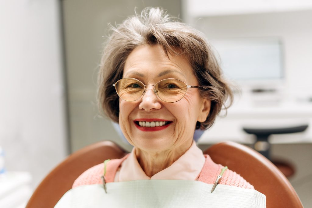 Elderly,Woman,With,Glasses,Smiling,While,Seated,In,A,Dental