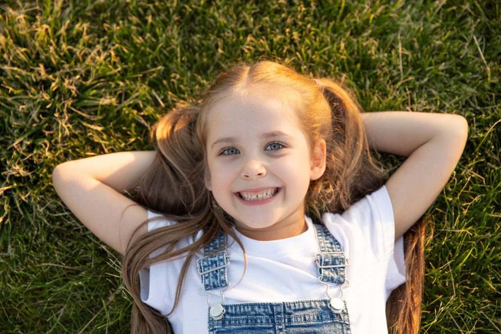 Top,View,Happy,Little,Girl,Lying,On,Grass,And,Smiling.
