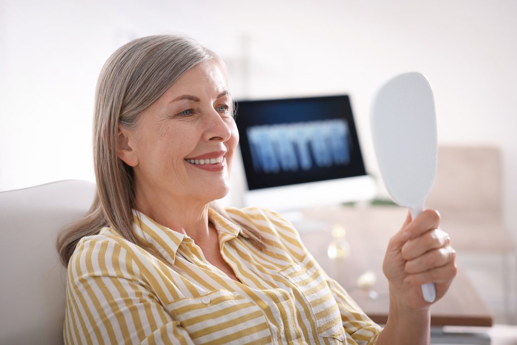 Senior,Woman,Looking,In,Mirror,At,Her,Teeth,With,Dental