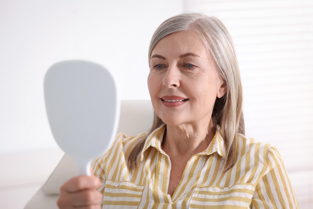 Senior,Woman,Looking,In,Mirror,At,Her,Teeth,With,Dental